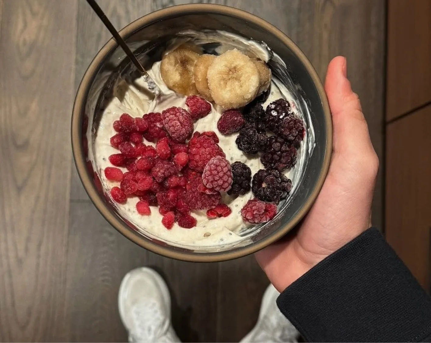A bowl of yoghurt topped with raspberries, blackberries and banana held in one hand