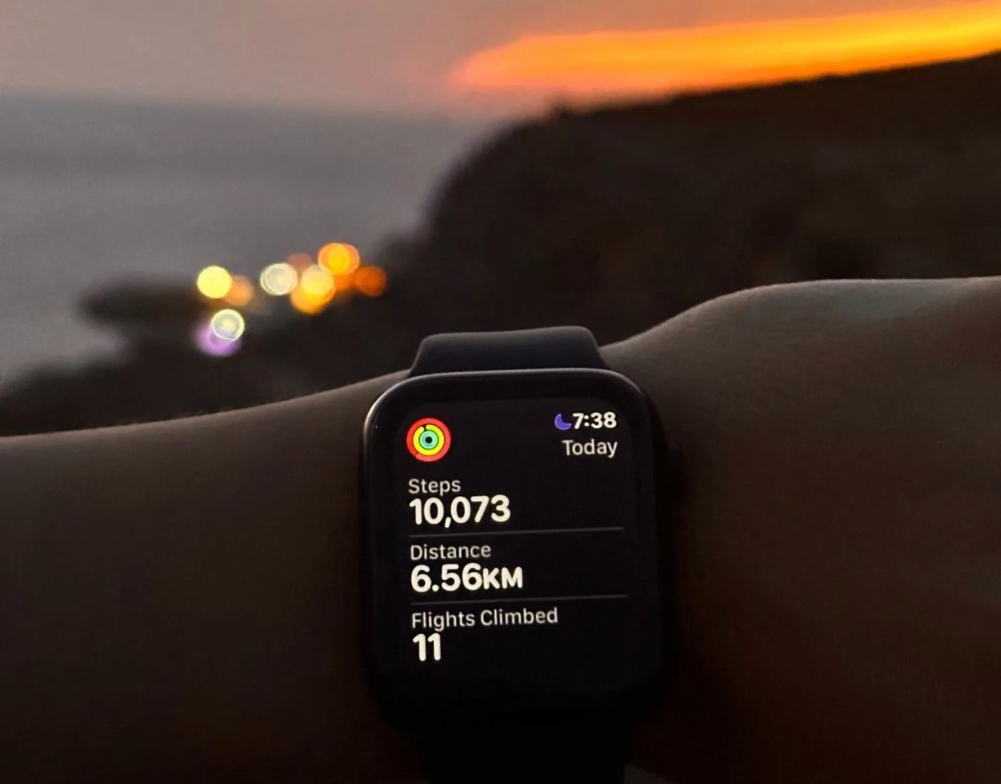A smartwatch on a wrist showing 10,073 steps and 6.56 km walked at sunset